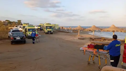 EPA On the beach, medic with a stretcher loaded with supplies on the bottom right. In the top left, multiple ambulance vans and some cars.