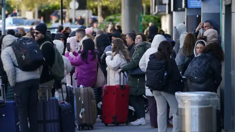 PA Media Dozens of people gathered outside an airport terminal building