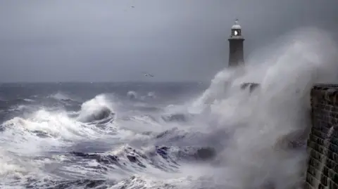 Getty Images Waves whipped up by a storm crash against a sea wall in Tynemouth, with a lighthouse in the background.