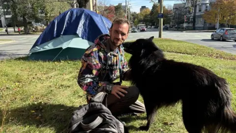 BBC Andrew Goodsell poses outside his tent with his dog in downtown Halifax