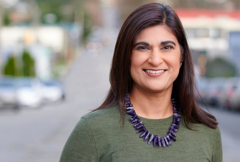 A woman smiling with shoulder length wearing a green top and purple beaded necklace.