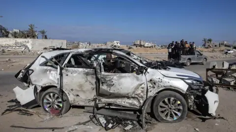 EPA The wreckage of a car seen following an Israeli strike in southern Gaza. The car is white but partially burned-out. It's roof is caved in, it is missing its windows, and its tyres are flat. 