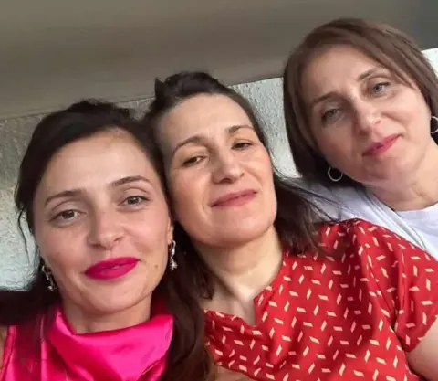 Tamuna Museridze Close-up of three women: Tamuna in a bright pink top, her half-sister who is wearing a red top and cousin who is in a white top. All three are smiling and have long, straight, dark hair.