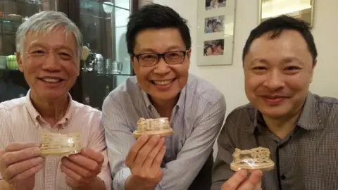 Chan Kin-man Chu Yiu-ming, Chan Kin-man and Benny Tai in 2013 smiling and holding up a birthday gift of wood carvings spelling out "persevere, peace, love"