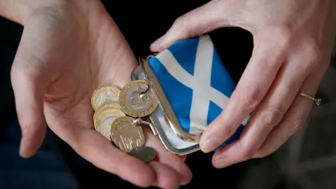 PA Media Coins being emptied out of a purse with a Saltire on it into someone's hands.