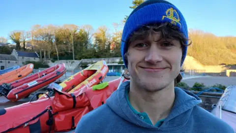 Finlay wearing a bobble hat is pictured next to a lifeboat at Atlantic College