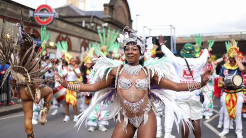 Reuters A black woman in a dazzling costume dances near a Tube station on the parade route