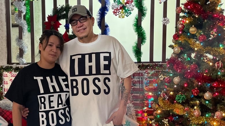 A picture of a man and a woman standing in front of a christmas tree inside someone's house.