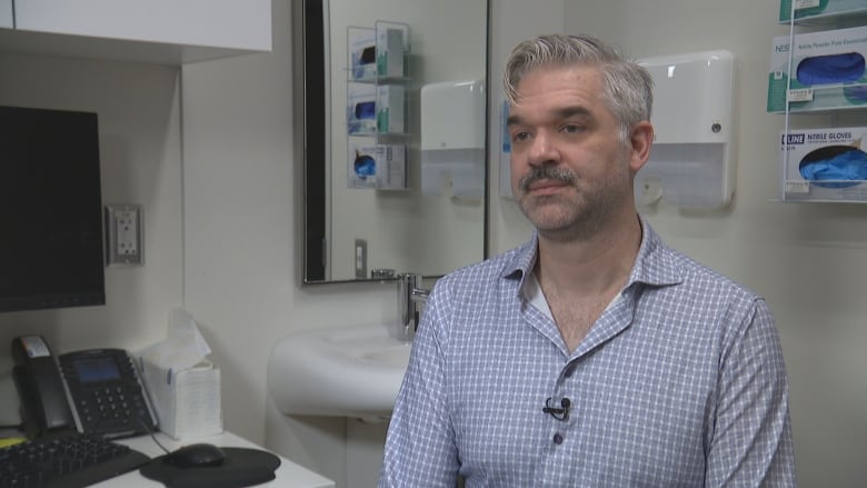 A man sits in a doctor's office while being interviewed. 