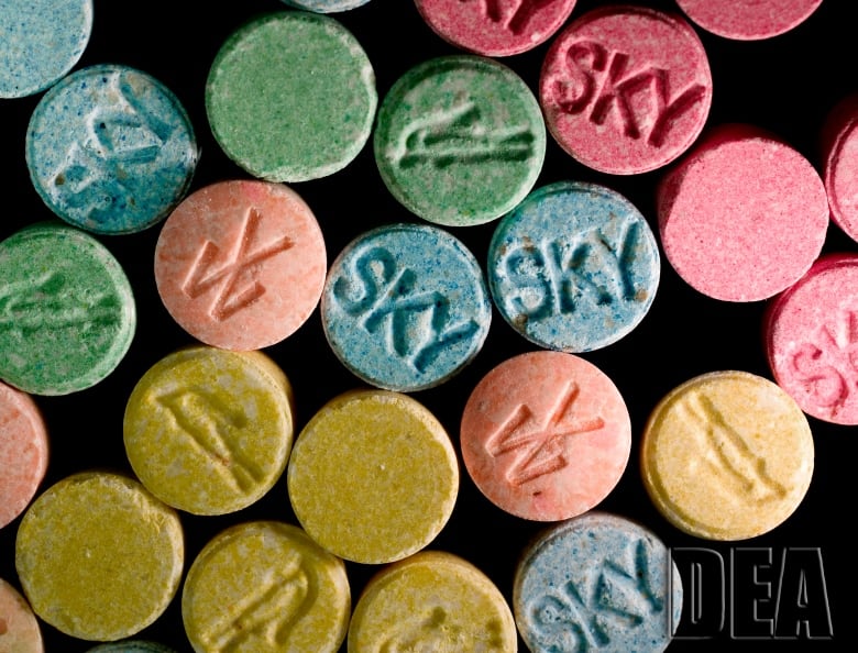 Roughly a dozen brightly coloured pills are seen on a black background. 