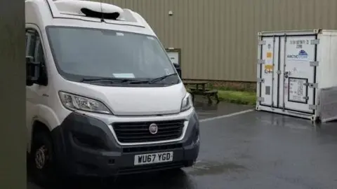 Tommy Banks The front of a white refrigerated van, parked on a business park.