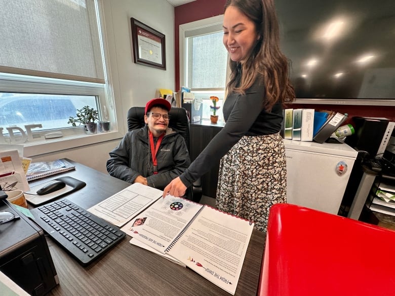 A woman standing over a man who is sitting at a desk