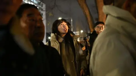 Getty Images A woman with a beige coat and long black hair shouts slogans as she protests outside parliament in Seoul