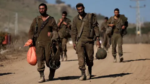 EFE/REX/Shutterstock Five Israeli soldiers, dressed in dark green army uniform and combat boots walk along a dusty road with their belongings as they return to Israel from Lebanon 