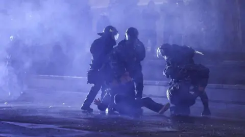 Getty Images Police bundle a protester in Georgia to the ground on a darkened street in the capital