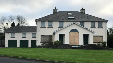 Clonduff parochial house which is a large residential building attached to parish offices.  The ground floor windows of the vacant building have been boarded up.