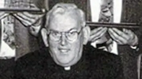 Pacemaker A black and white photo of the late Fr Malachy Finegan.  He is wearing glasses, a black suit and a priest's collar.