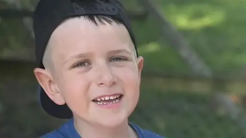 Family handout Archie York. He is wearing a backwards facing, black baseball cap and is smiling at the camera. A tuft of his fringe is poking out form under the hat.