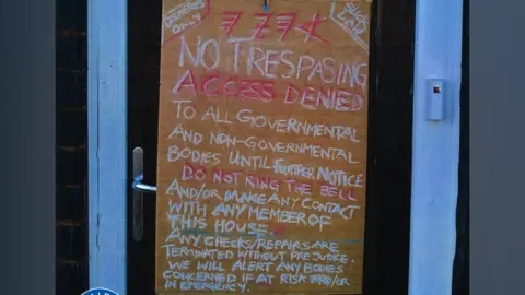 West Midlands Police A large sign on a front door which reads "no trespasing, access denied to all governmental and non-governmental bodies until further notice. Do not ring the bell and/or make contact with any member of this house. Any checks/repairs are terminated without prejudice. We will alert any bodies concerned if at risk and/or in emergency"