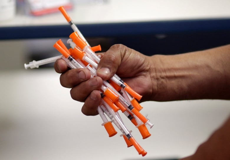 A hand holding a fistful of syringes and needles.