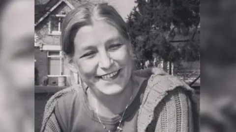 Dawn Sturgess smiling at the camera. It is in black and white and she is wearing a thick cardigan and a silver necklace.