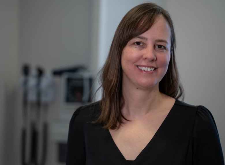 A female doctor with long, brown hair standing in a medical office. 