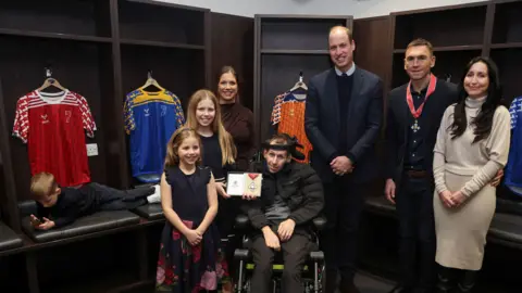 PA Media HRH Prince William, flanked by Burrow and Sinfield and their wives, with Burrow's two daughters and his son (playing on a mobile phone) in a team dressing room