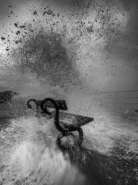 Adam Bullock A wave breaks against a bench on the sea front