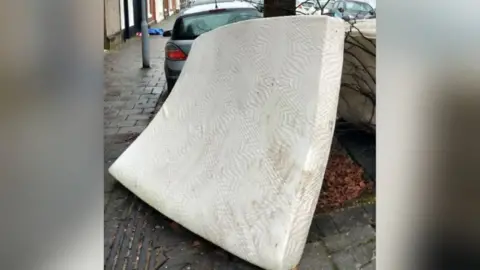 A fly-tipped mattress dumped against a tree in Cardiff