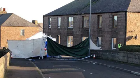 Police at scene of death in Peterhead, police officer standing outside house, street covered up .