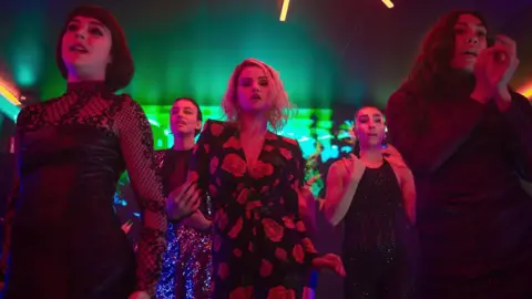 Netflix Selena Gomez in the centre of a group of women dancing with nightclub-style green and red lights