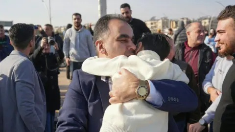 Getty Images A man embraces a child at the entrance of Aleppo city, on December 9, 2024, as people wait for the return of relatives after the release of detainees from Syrian government prisons following the ousting of Syria's president.