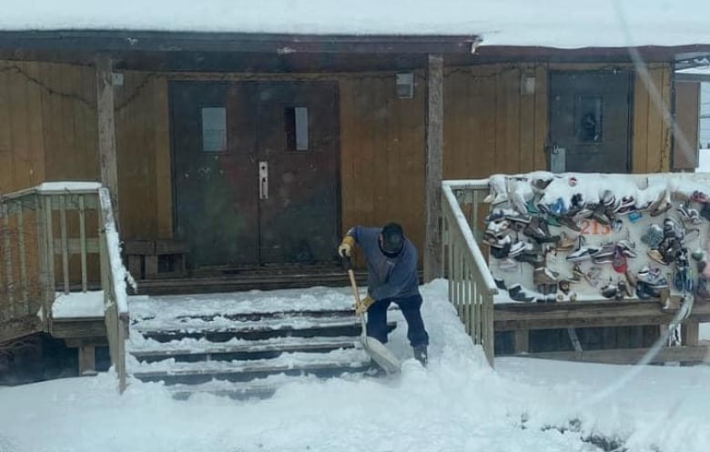 A man shovels the snow fro the steps of a building. 