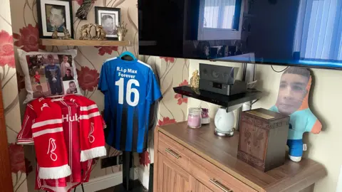 Leanne Ekland A cushion with pictures of teenager Max Dixon next to football shirts and a television. There is also a teddy with Max's face on it.