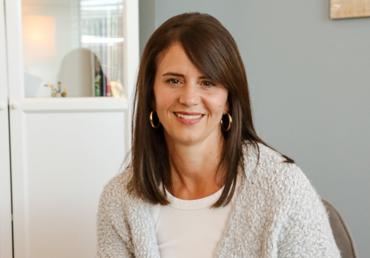 A woman with brown hair and grey cardigan sweater is smiling at the camera. 