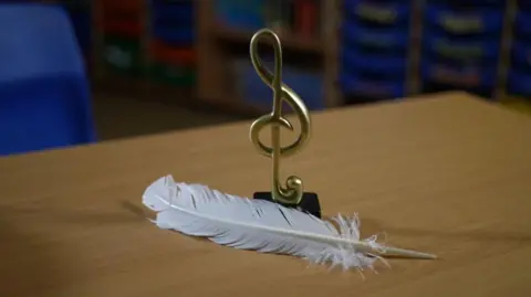 A white feather and a gold music award on a wooden table. 