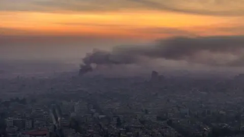 Getty Images Smoke rises from an aerial view of Damascus city with sunlight in the background