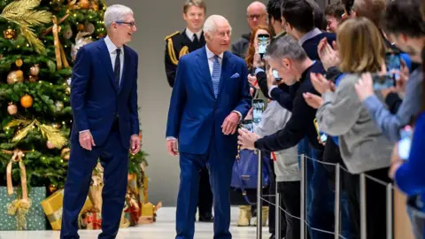 Getty Images The King and Tim Cook walk along an aisle lined with members of the public, with a Christmas tree in the background