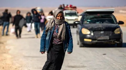 Getty Images Displaced Syrian Kurds walk along the road as they flee