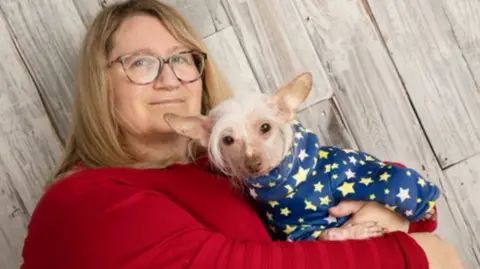 Imageexclusive.co.uk/ParrotPrint Bev wearing a red sweater holding Muppet- who is wearing a blue dog coat with yellow and white stars on it. 