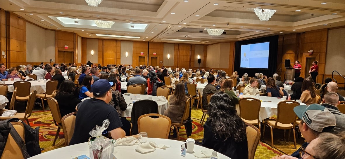 A group of people are sitting in a large hotel conference room. 