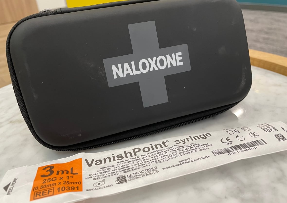 A naloxone kit, syringe wrapper and sharps collector are displayed on a table.