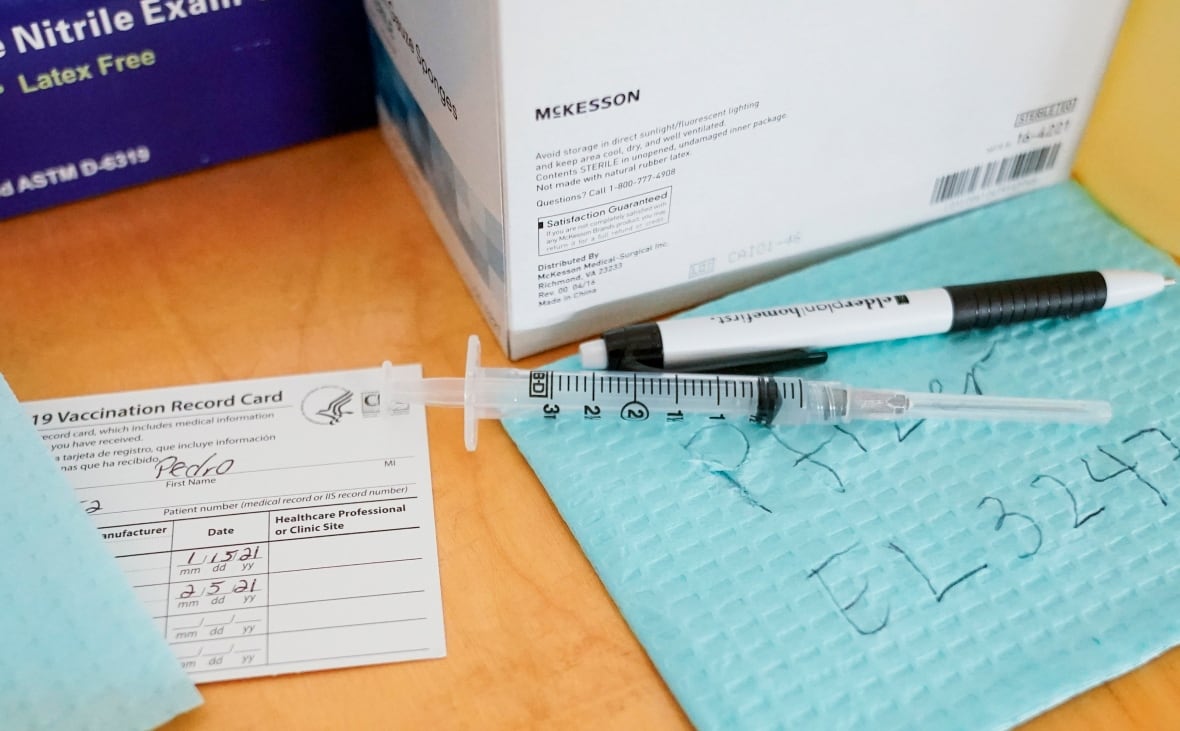 A syringe filled with a COVID-19 vaccine is seen alongside its batch number a patient's vaccination card. 