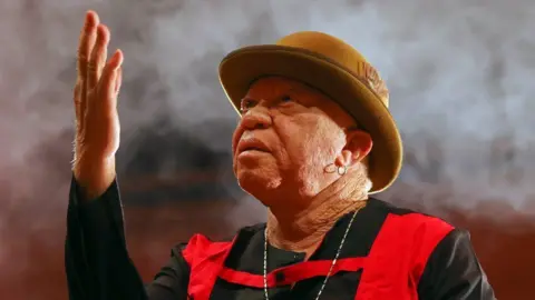 Getty Images Salif Keïta giving a concert in Ankara, Turkey - 2022. He's wearing a beige bowler hat and a black and red outfit