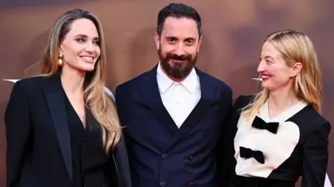 Getty Images (L-R) Angelina Jolie with director Pablo Larraín and co-star Alba Rohrwacher. All three are smiling.