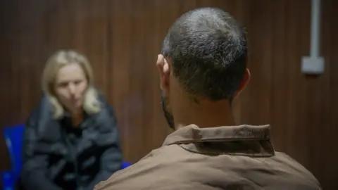 BBC/Michael Steininger Al Sina IS inmate sits with his back to the camera, facing reporter Orla Guerin who is out of focus