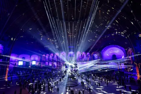 Stephane De Sakutin/AFP People skate on the indoor ice rink at the Grand Palais des Glaces, in Paris. A large reflective ball stands in the centre, with lights shining on to it from the walls and roof of the building.