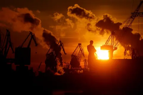 Anatoly Maltsev/EPA-EFE A giant monument to explorer Admiral Ivan Kruzenshtern is silhouetted at sunset in freezing-cold St Petersburg, in Russia. Cranes and clouds are also silhouetted against the orange sky.