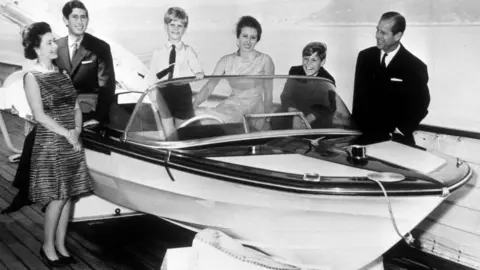 PA Media The royal family's 1969 card features a black-and-white photograph of them gathered around a speed boat on land. All are smartly and formally dressed and smiling. The Queen, the Duke of Edinburgh and Prince Edward are standing. Prince Charles, Princess Anne and Prince Andrew are sitting.