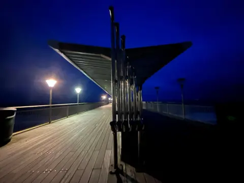 Jojo Arnell A shelter on a pier; one side is lit, the other in darkness